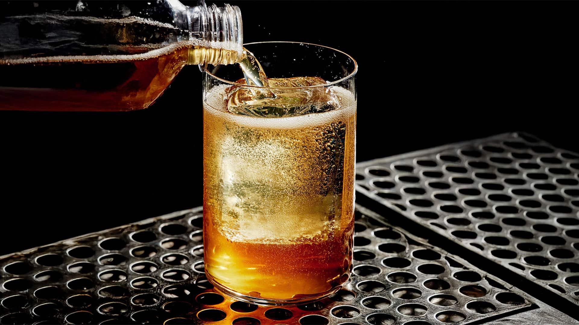 Liquid from a bottle being poured into a glass with ice.