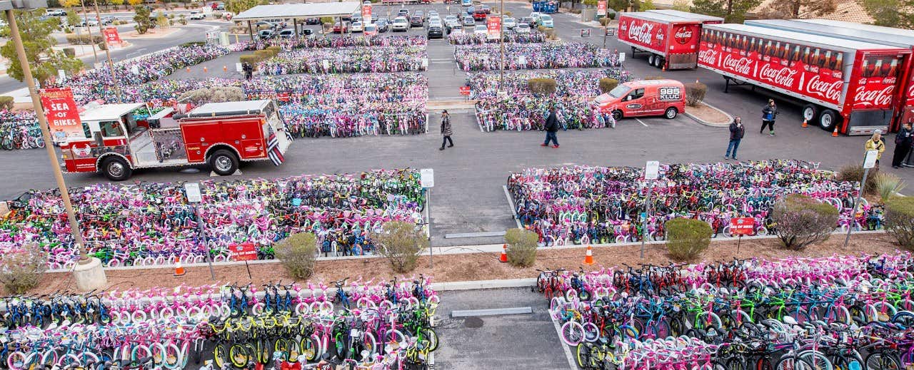 A large parking lot filled with rows of bicycles, a fire truck, Coca-Cola trucks, and people walking around.