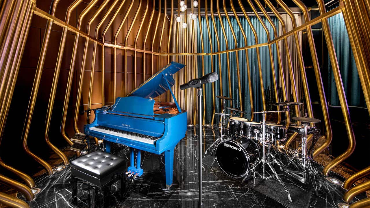 A bright blue piano and drum set inside a gold cage as a stage.