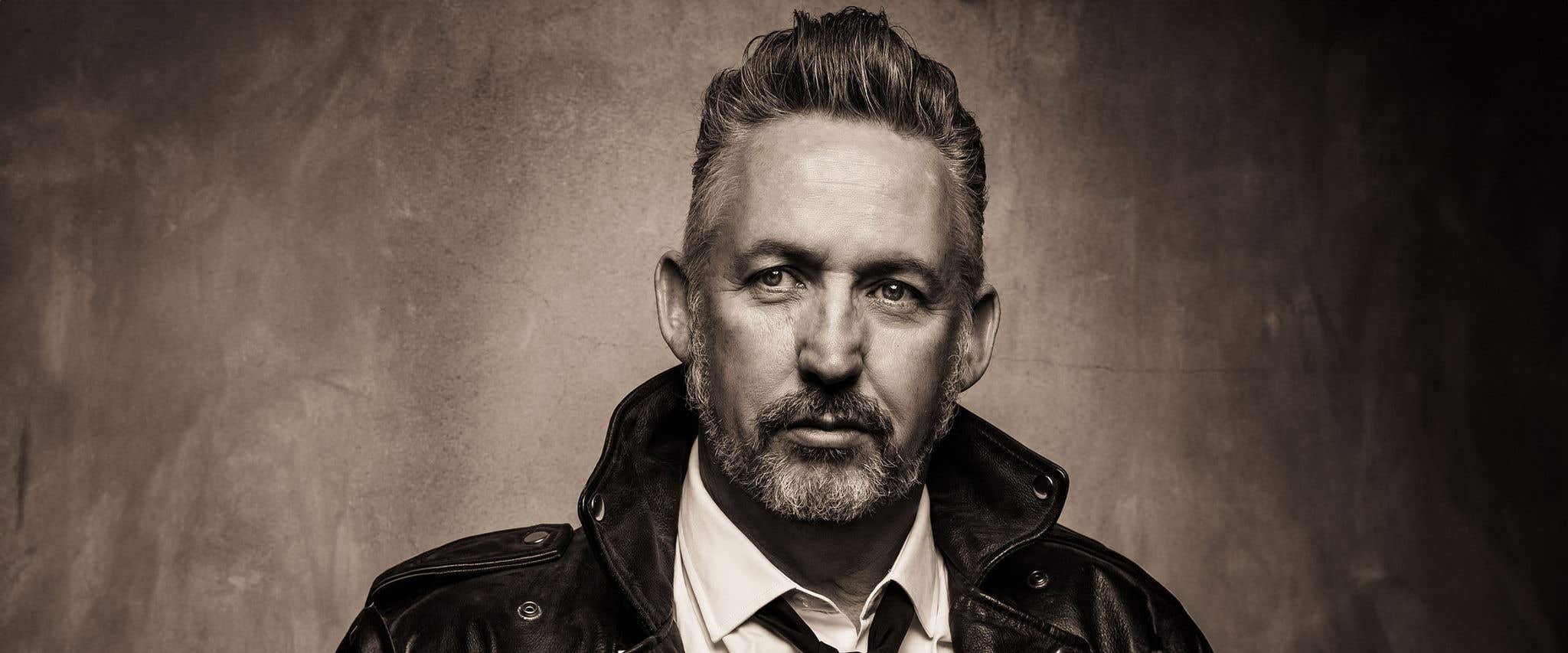 Black and white portrait of Harland Williams in white collared shirt, black tie and leather jacket.