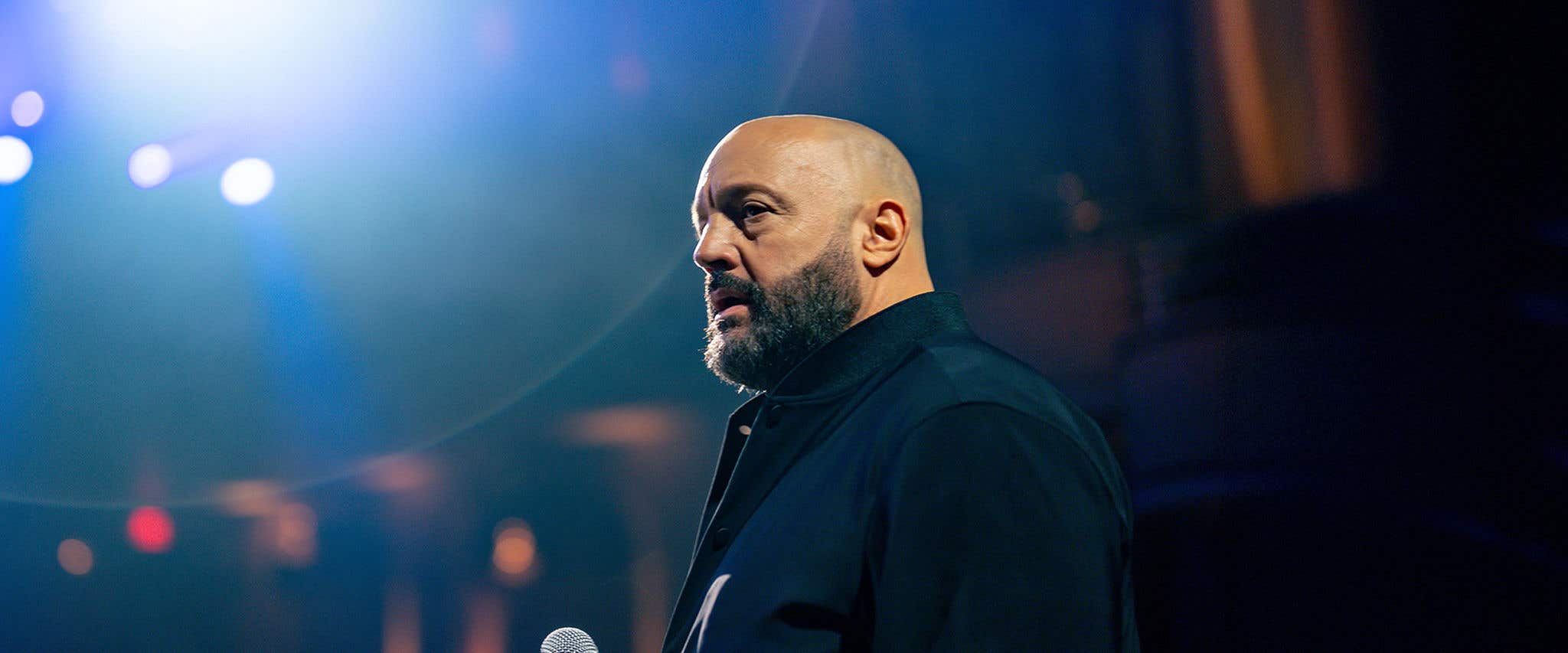 Comedian Kevin James on stage holding a microphone.