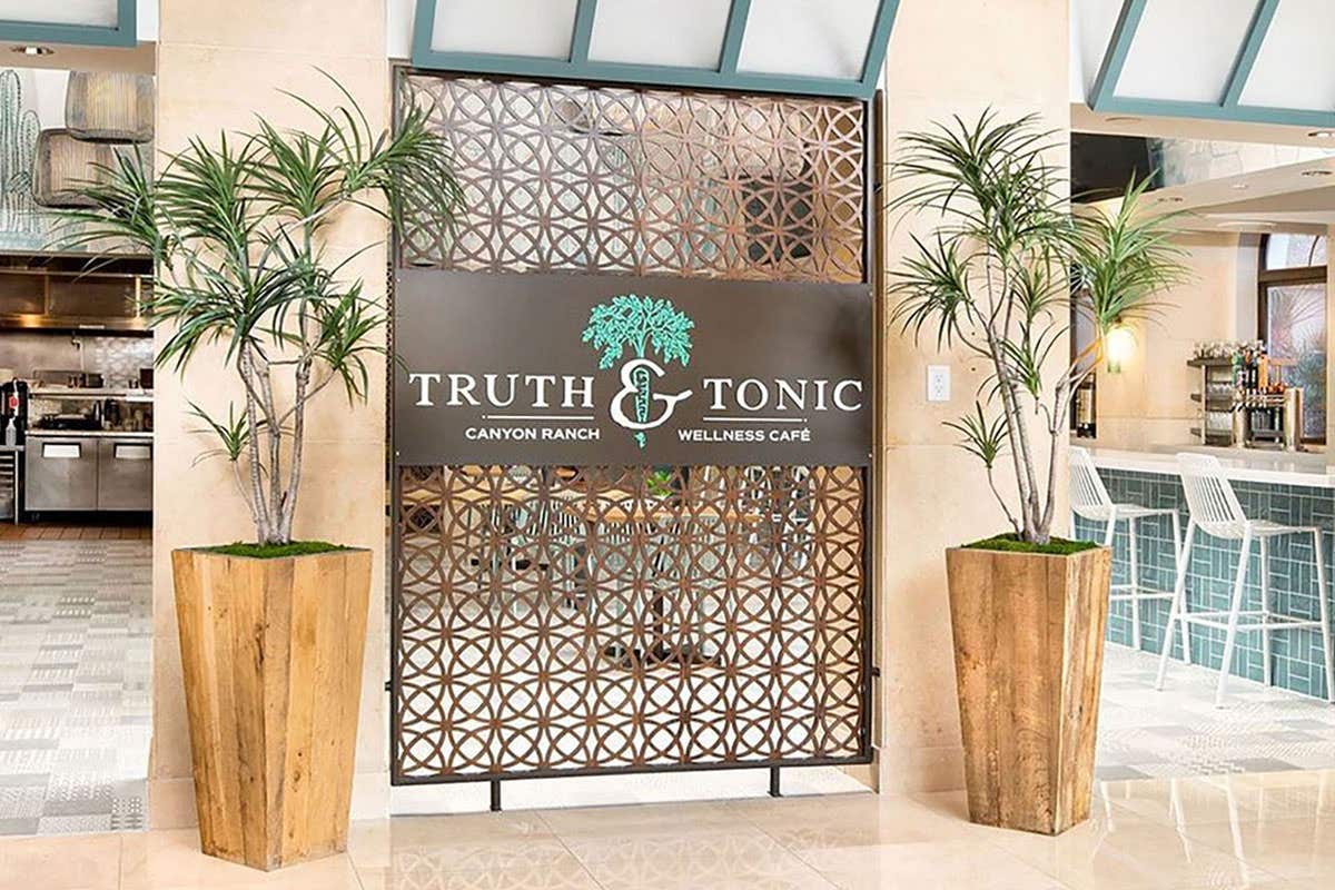 Entrance to Truth & Tonic Wellness Café with a decorative wooden screen and two large potted plants on each side.