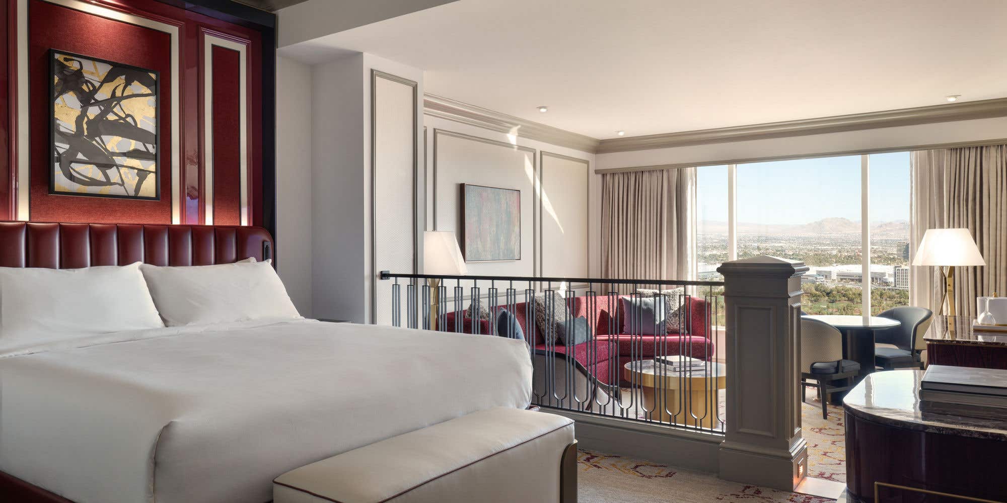Newly Remodeled Luxury King Suite with a white bed, abstract art, and a living area with a red sofa, framed by a large window showing a city view.