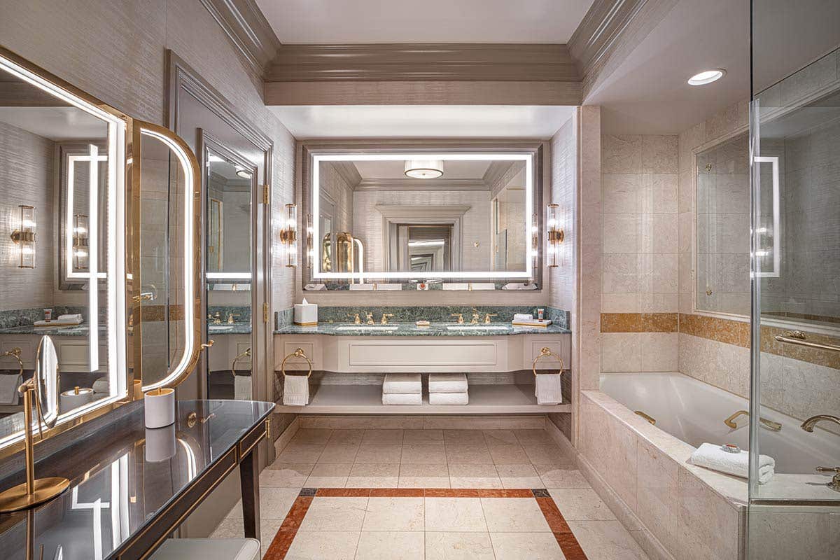 Newly remodeled bathroom with large bathtub, dual-basin sinks, granite countertops, and a large illuminated mirror. 