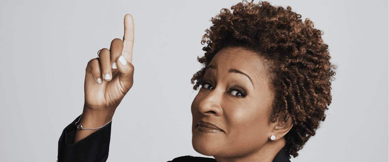 Wanda Sykes against a light gray backdrop pointing up
