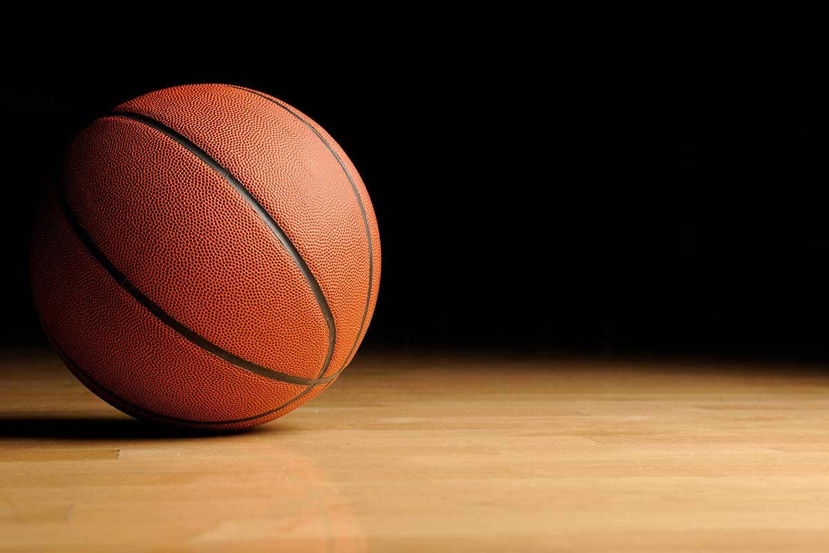 A basketball resting on a wooden court with a dark background.