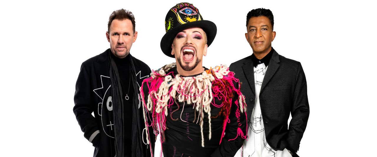 Boy George & Culture Club standing in front of blank white background staring at the camera.