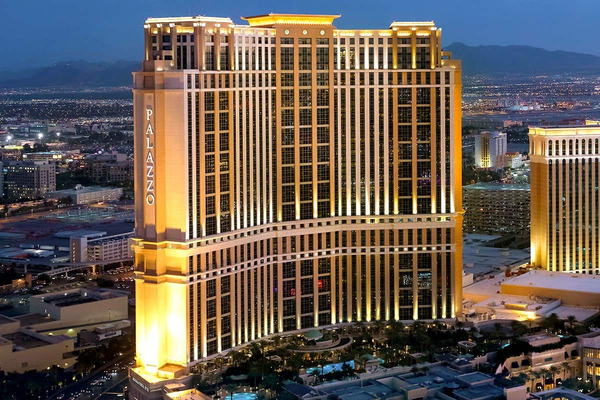 Aerial view of The Palazzo hotel and resort in Las Vegas illuminated at dusk, with city lights and mountains in the background.