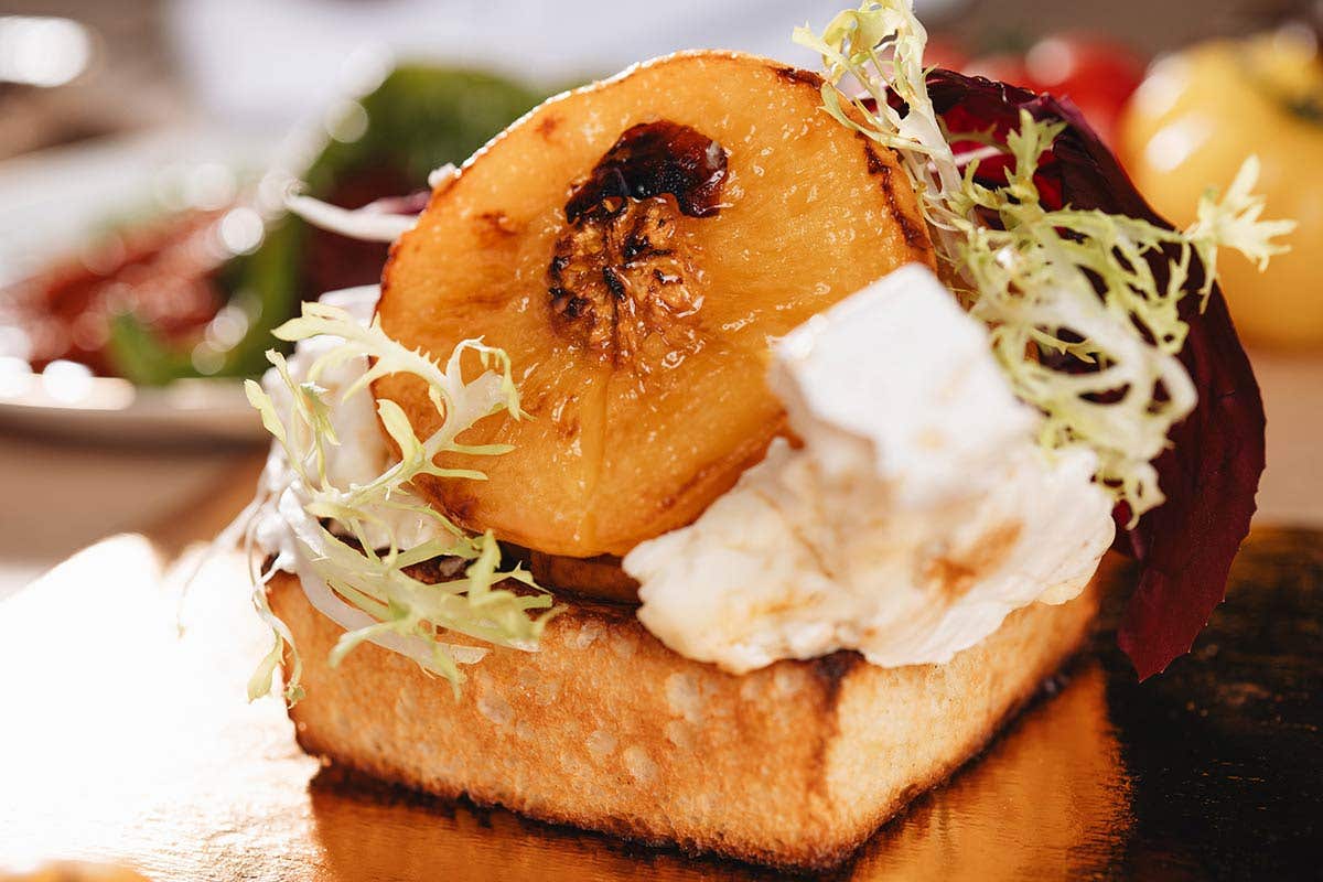 Roasted peach and ricotta on a piece of bread along with some greens