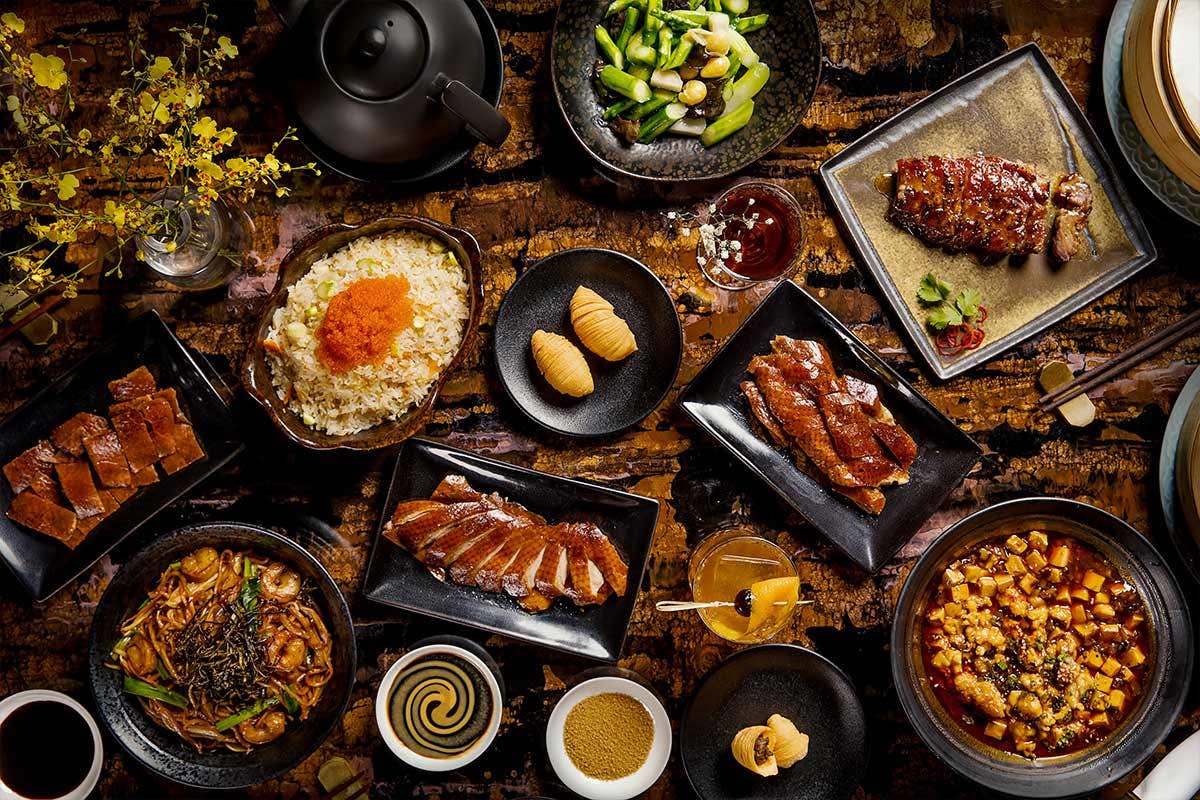 An overhead view of a lavish spread of various Asian dishes on a dark wooden table.