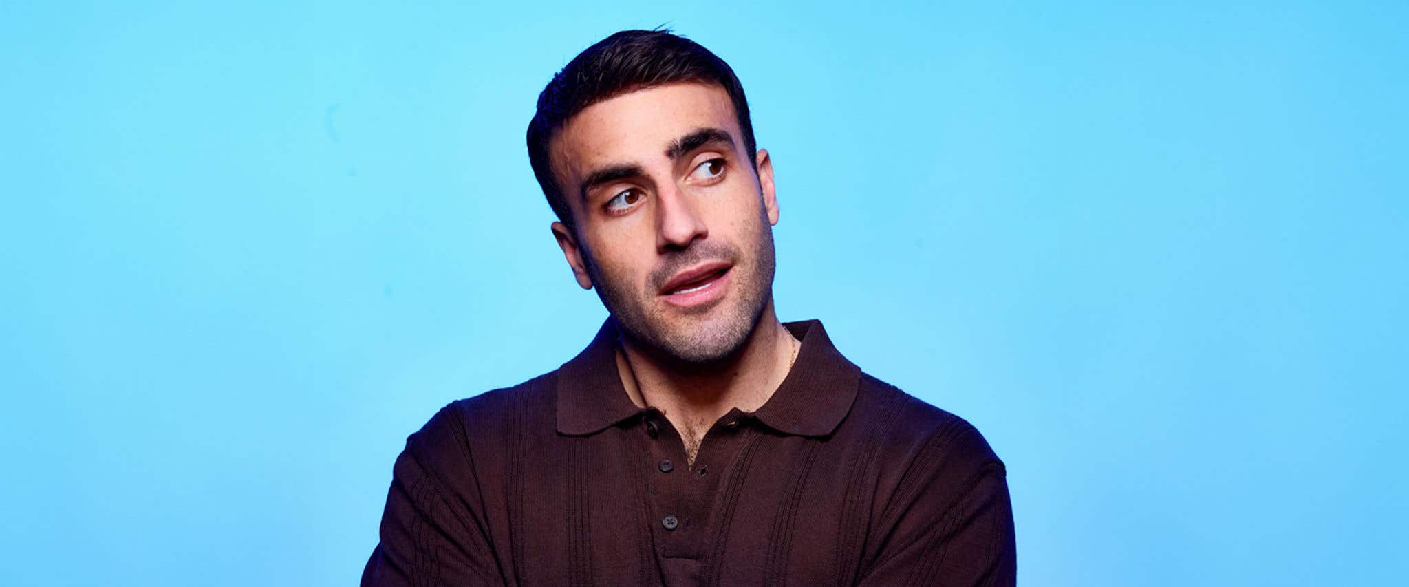 Rob Anderson in a brown collared shirt in front of light blue background looking off to the side.