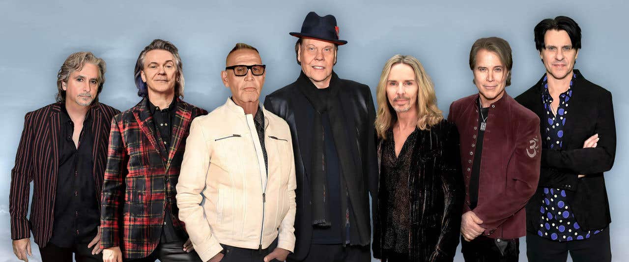 Styx band members standing together in front of a cloudy gray background. 
