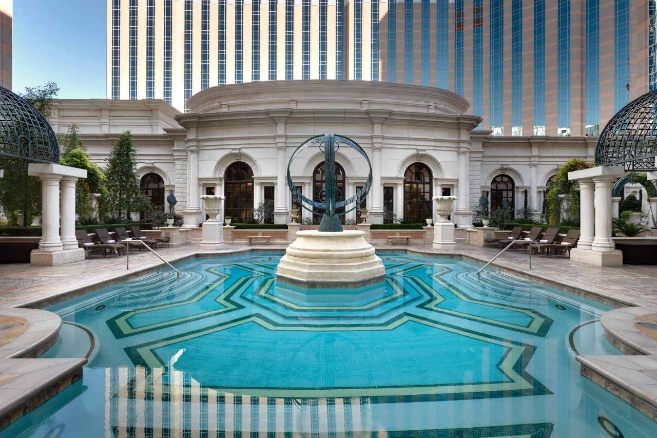 Luxurious circular pool with sculptural centerpiece, surrounded by ornate architecture and tall buildings in the background.