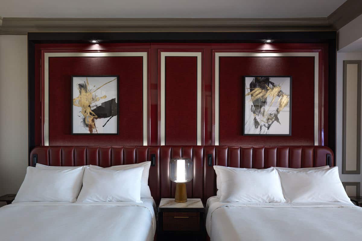 Two queen beds in a hotel room with a red leather headboard with artwork above each bed.