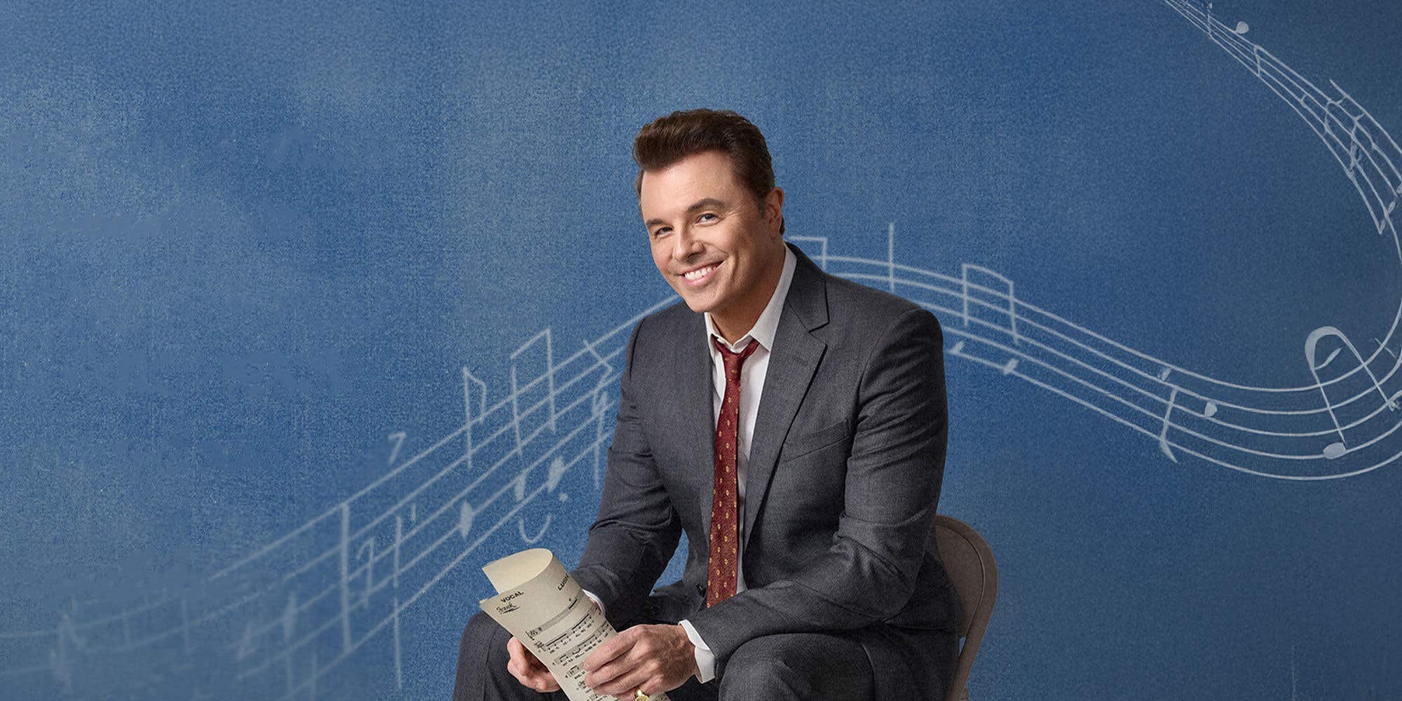 Actor and singer Seth MacFarlane sitting on a folding chair, set against a blue background with music notes.