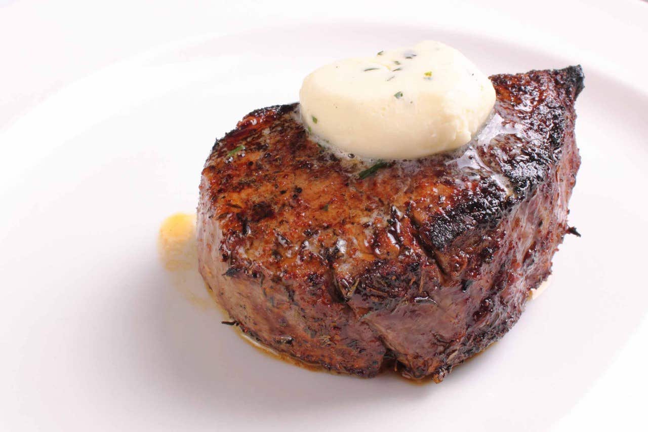 Grilled steak topped with a melting pat of herb butter, served on a white plate.