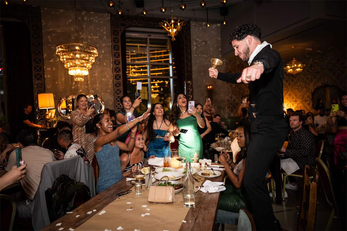 A diner dancing on his chair at a restaurant with lots of excited diners taking photos and cheering in the background