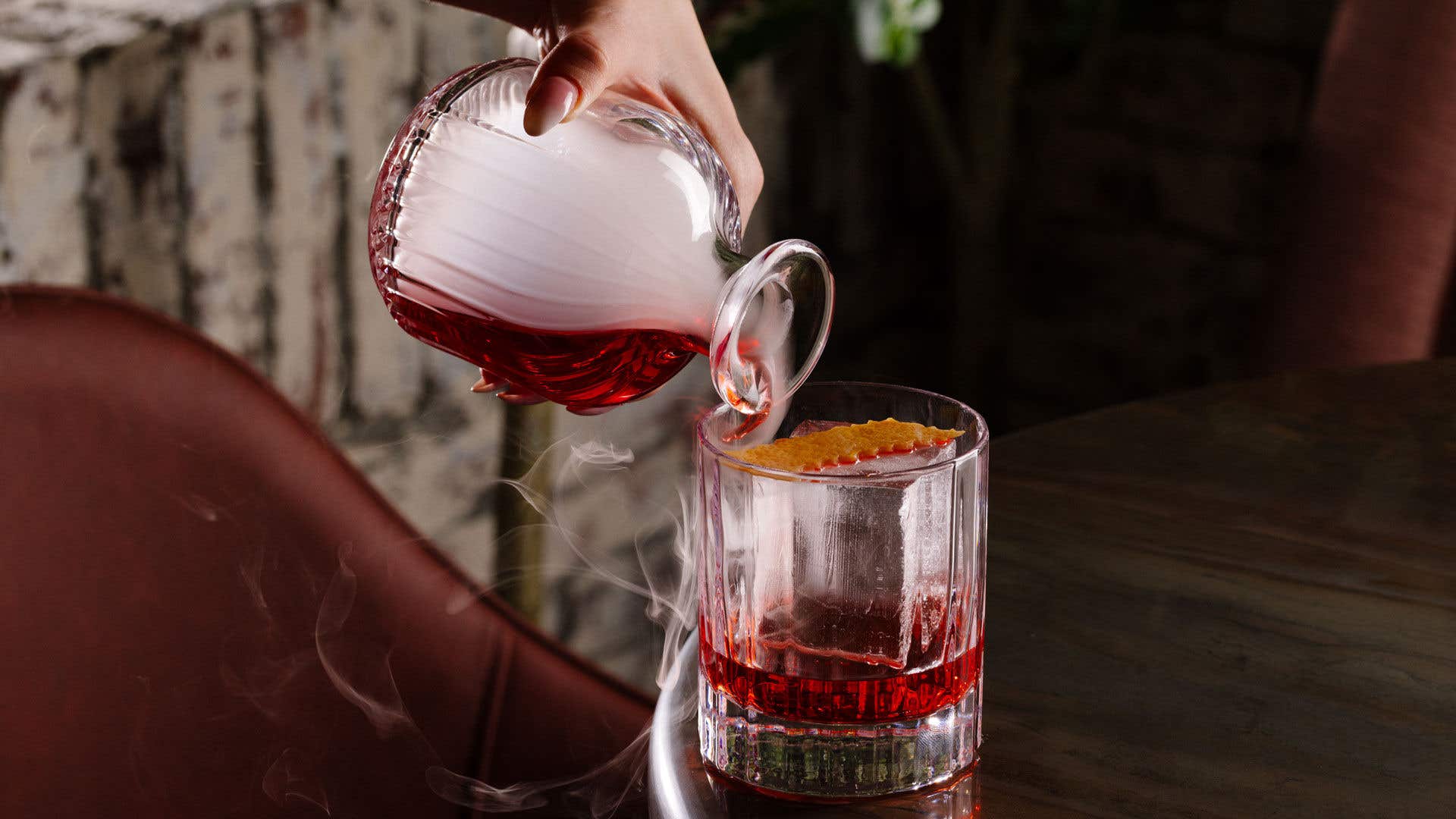 Whiskey drink being poured from a carafe into a glass with a cube ice mold.