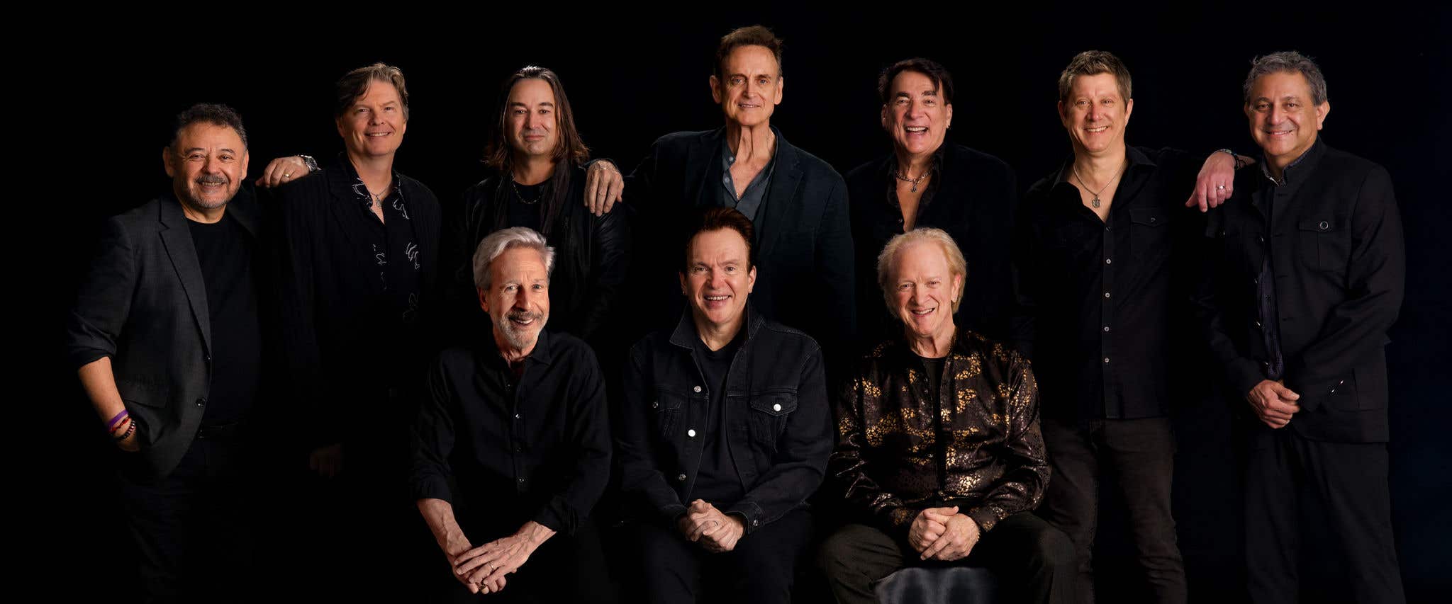 Chicago band members posing together in front of black background looking at the camera. 