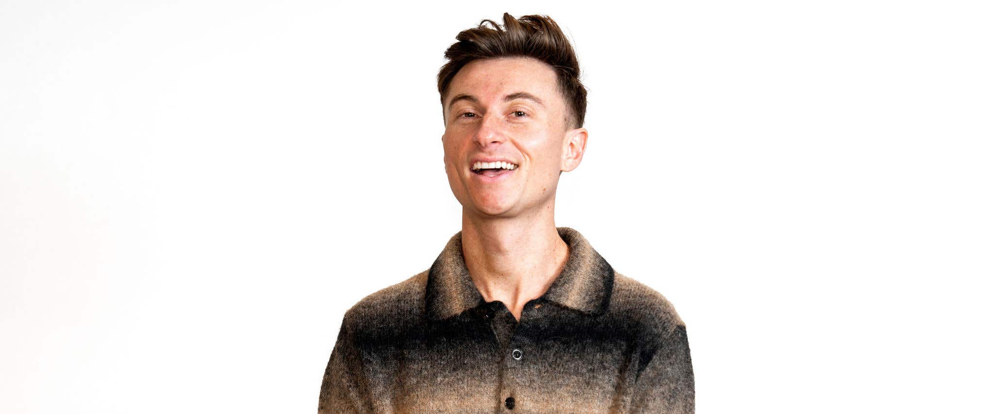 Trevor Wallace smiling and wearing a brown and black striped collar shirt in front of all white background. 