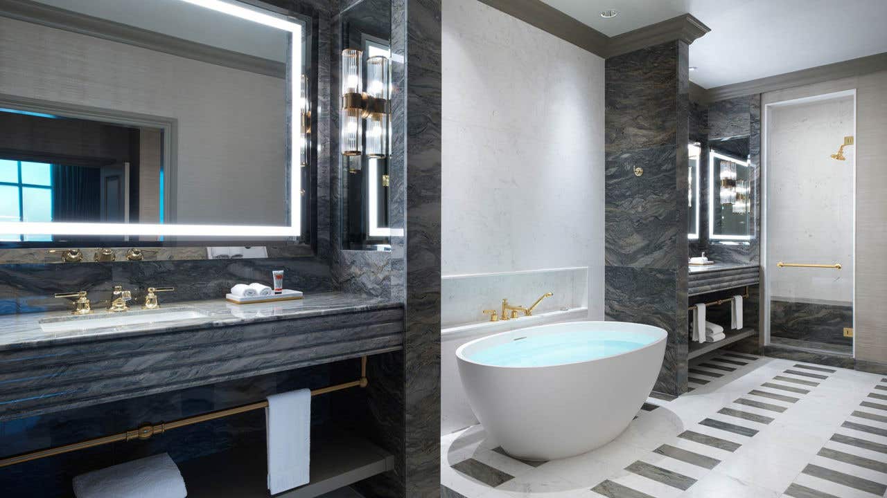 A hotel bathroom with two separate sink vanities, a Roman tub in the middle, and a shower to the right.