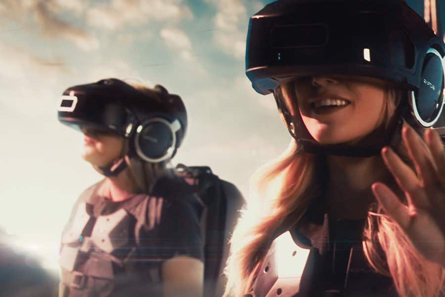 Two people wearing VR headsets, smiling, and enjoying a virtual experience with a bright sky background.